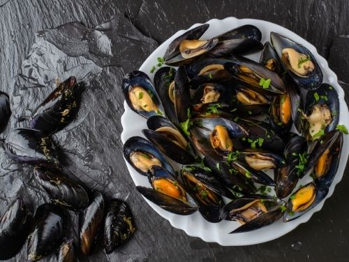 Foto di un vassoio di cozze cotte con di fianco cozze crude
